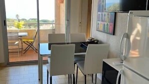 Cozinha com geladeira, mesa de jantar com cadeiras e TV fixada na parede.