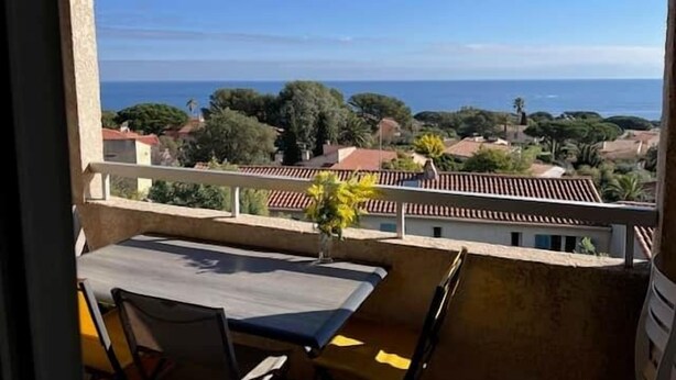 Uma varanda com mesa e cadeiras, com vista para uma área costeira com casas e árvores.