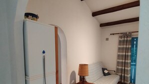 A room with a tiled floor, a bed with a patterned bedspread, a small table with a lamp, and a white door with a decorative handle. - Petit Mas: ideal for families, garden, swimming pool, sea 15' away (Cavalaire-sur-Mer)