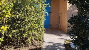 A pathway leading to a building with a blue door, surrounded by greenery and a tiled roof. - Petit Mas: ideal for families, garden, swimming pool, sea 15' away (Cavalaire-sur-Mer)