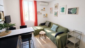 Un ambiente compatto con zona pranzo, divano, un piccolo sgabello e televisore.