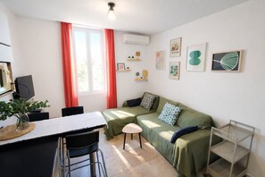 Ein kompakter Wohnbereich mit Essplatz, einer Couch, einem kleinen Hocker und einem Fernseher.