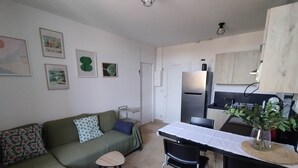 Un ambiente compatto con un divano, un piccolo tavolo, un frigorifero e un angolo cottura.