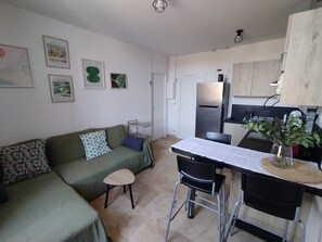 Ein kompakter Wohnbereich mit Sofa, kleinem Tisch, Kühlschrank und Küchenzeile.