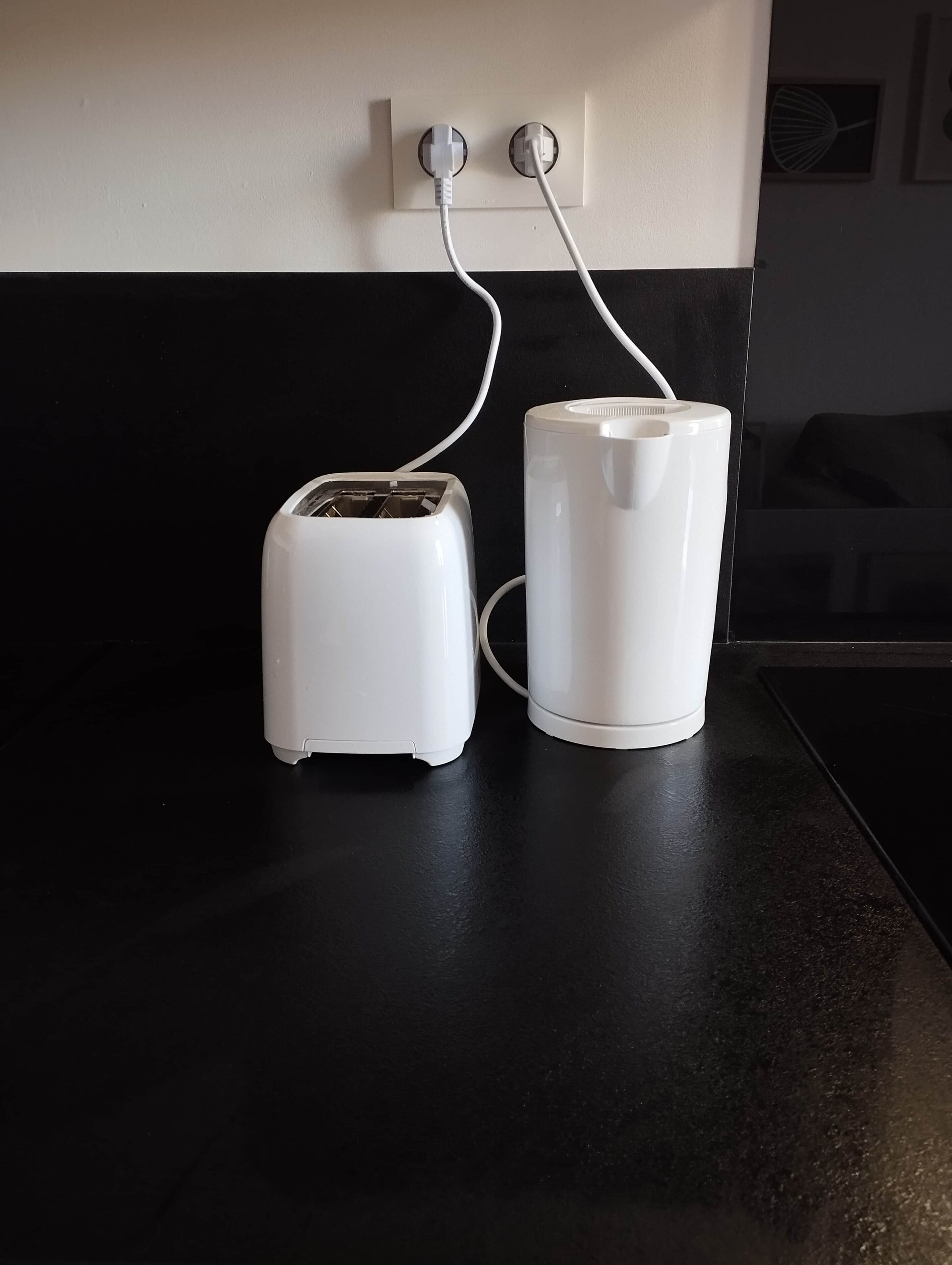 A kitchen with a toaster and a white mug on a black countertop, connected to a power outlet.