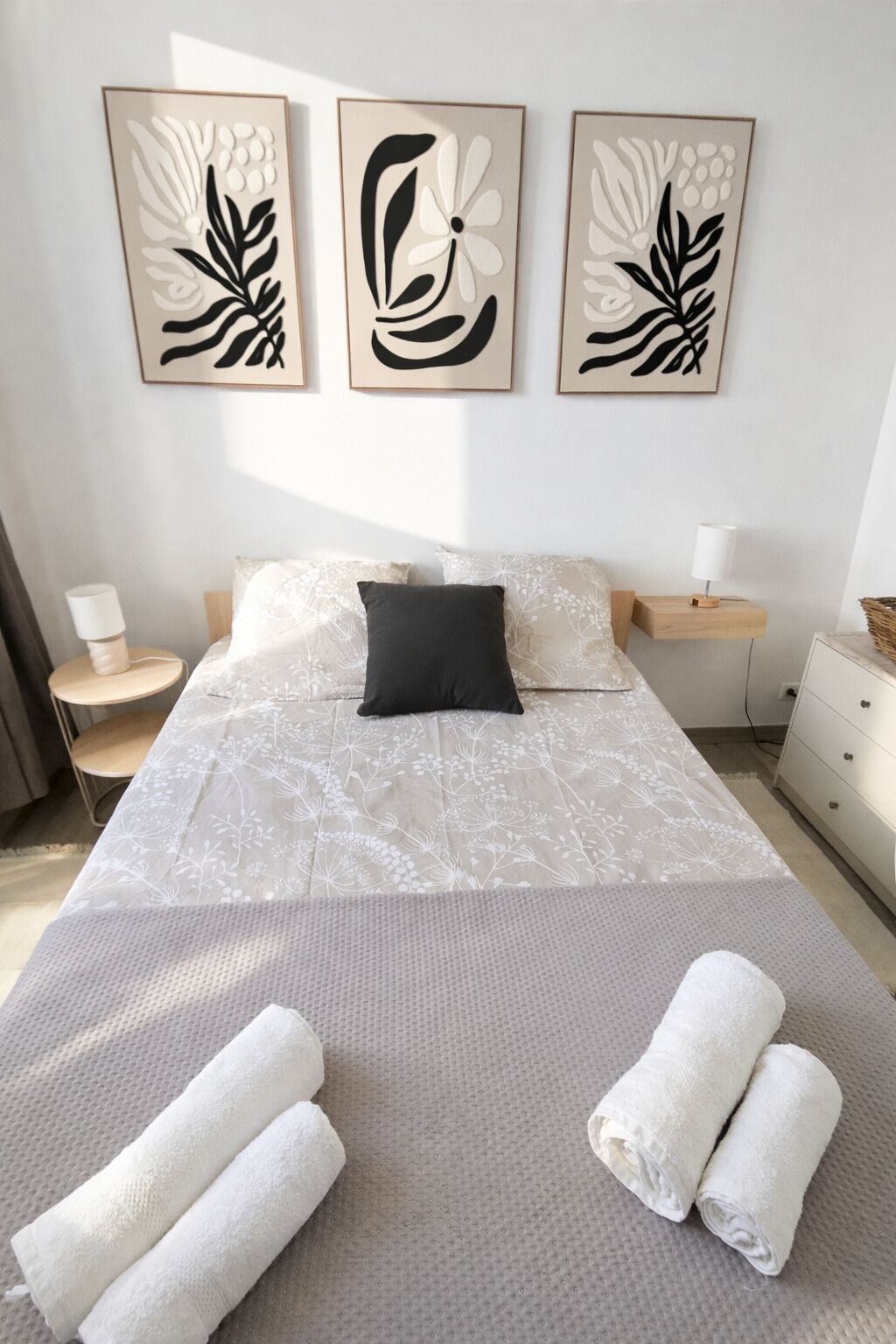 Una camera da letto con un letto, cuscini, un comodino, una lampada e opere d'arte alle pareti.