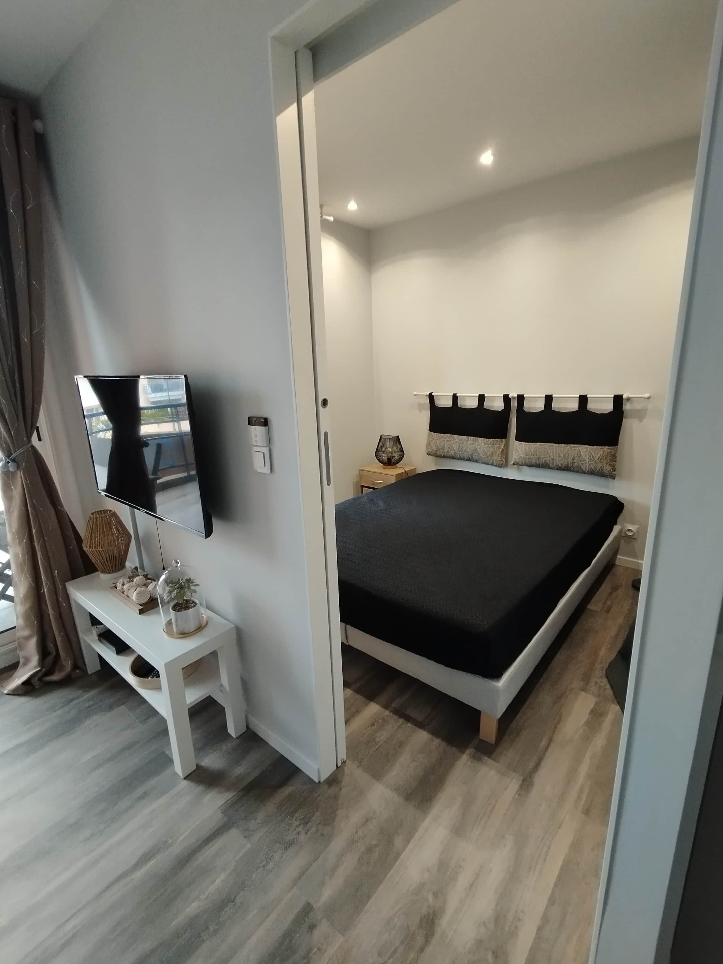 Une chambre à coucher moderne avec un lit, une table de chevet, une lampe et un téléviseur fixé au mur.