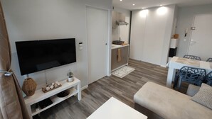 Un salon moderne doté d’un téléviseur à écran plat, d’une table basse blanche, d’un canapé beige et d’un coin repas avec une table et des chaises.