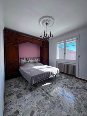 A bedroom with a bed, a chandelier, a window with blinds, and a radiator. - La Bastide des Gayants : garden, swimming pool, wifi (Le Luc)