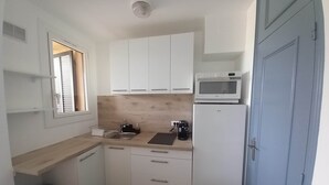 Cocina compacta con armarios blancos, microondas, cafetera y pileta.