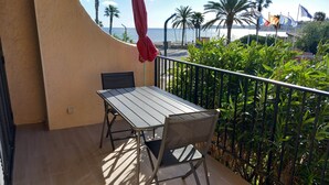 Un balcón con mesa y sillas, con vista a una playa con palmeras y banderas.