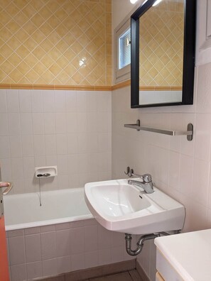 A bathroom with a white sink, a mirror, and a bathtub. - Exceptional sea view! Terrace, Private garage, Walking distance to the beach (Le Lavandou)