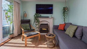 Un salon comprenant un canapé, un fauteuil, une cheminée et un téléviseur fixé au mur.