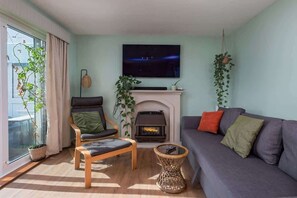 Ein Wohnzimmer mit Sofa, Sessel, Kamin und Wandfernseher.