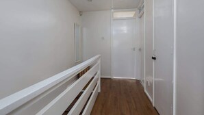 Un couloir aux murs blancs, doté d’un plancher en bois, d’une rambarde blanche et d’une porte au fond.