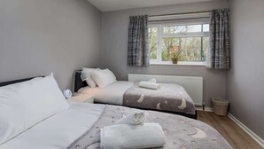 Une chambre avec deux lits, une fenêtre avec des rideaux, un radiateur et une plante en pot.