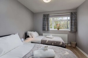 Ein Schlafzimmer mit zwei Betten, einem Fenster mit Vorhängen, einem Heizkörper und einem Blumentopf.