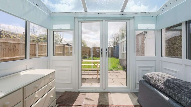 Une pièce dotée d’une grande porte-fenêtre coulissante donnant sur un patio, d’une commode blanche et d’un banc.