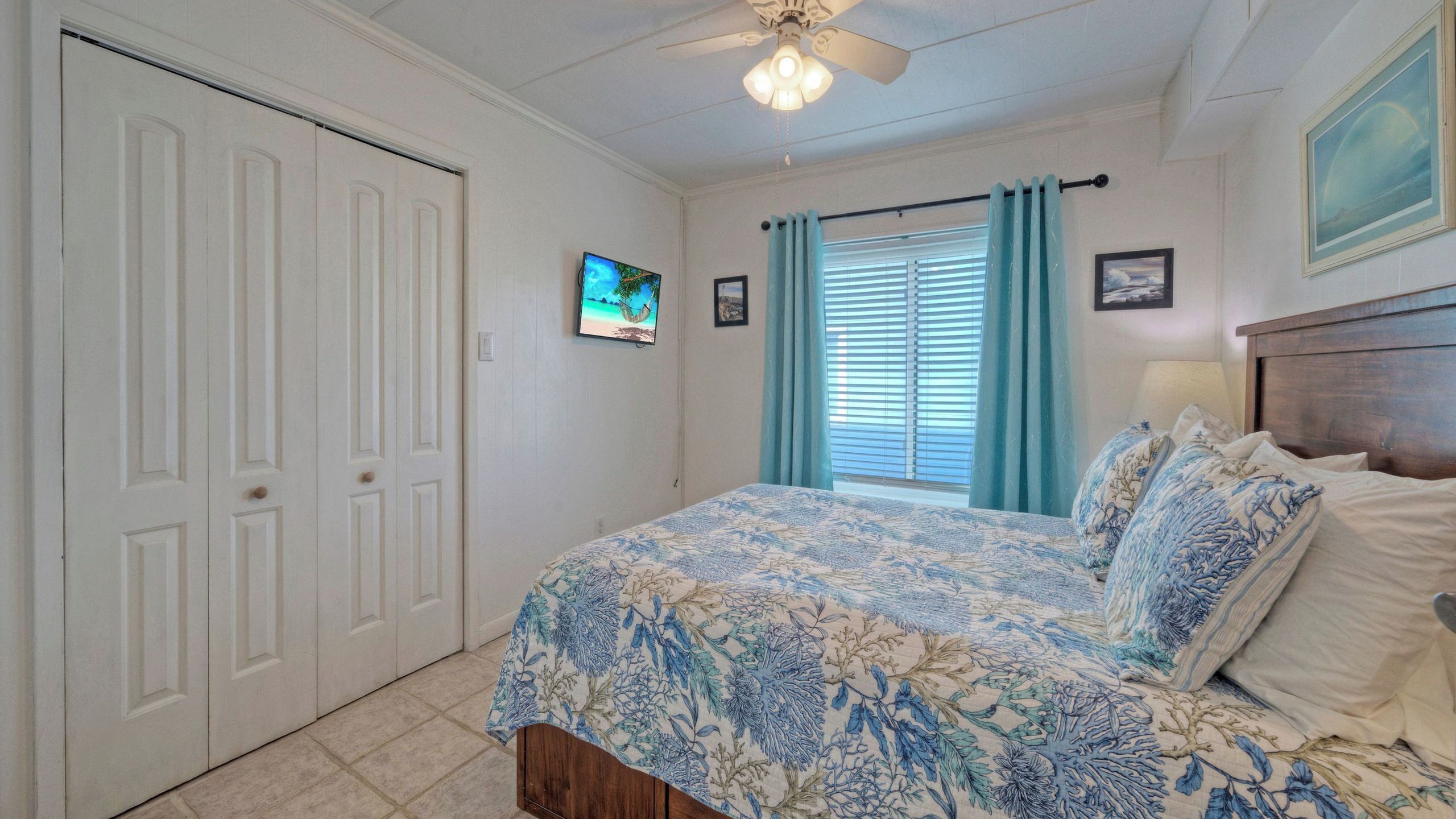 A bedroom with a bed, a ceiling fan, a window with curtains, and a door.