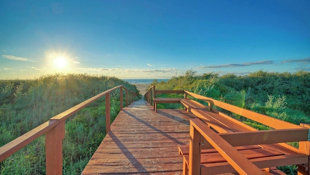 Un paseo marítimo de madera que lleva a una playa con cielo despejado.