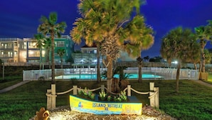 Vista nocturna de un resort con piscina, palmeras y un cartel que dice 'Island Retreat'.
