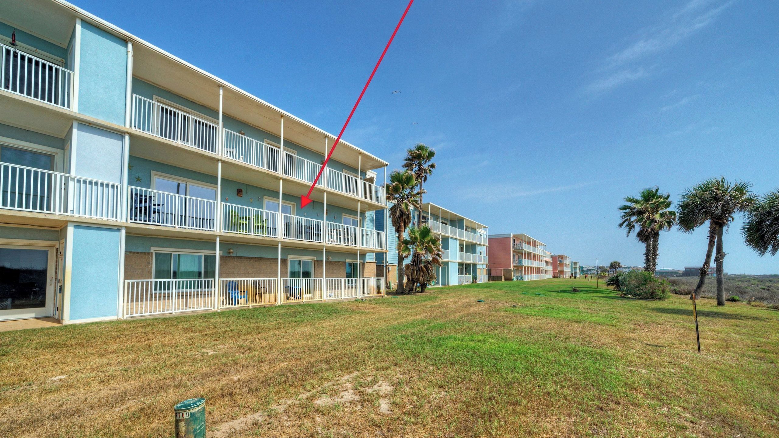 A multi-story hotel with balconies, a grassy lawn, and palm trees.