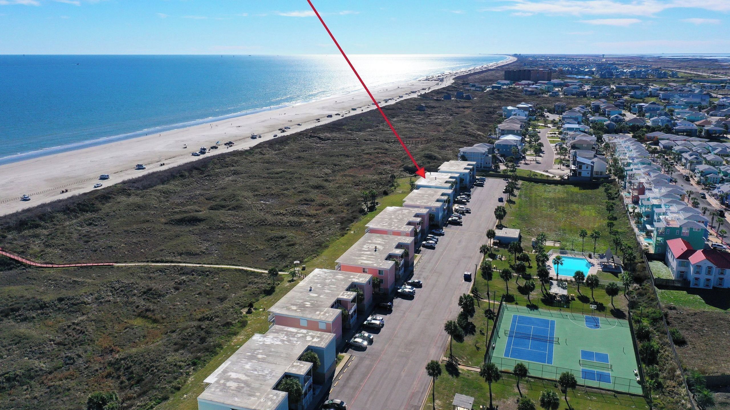 Zona residencial costera con playa, una hilera de casas de una sola planta y una cancha de tenis.