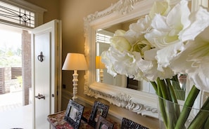 Ein Zimmer mit Spiegel, Lampe und Blumen in einer Vase.