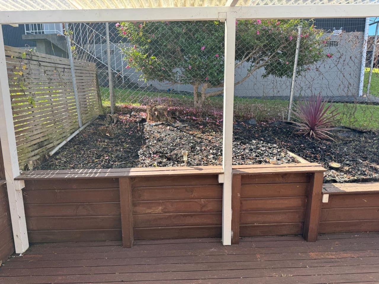 A wooden raised garden bed with a metal fence and a tree in the background.