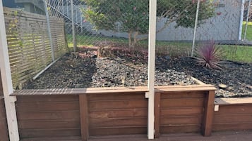 A wooden raised garden bed with a metal fence and a tree in the background.
