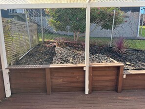 Una jardinera elevada de madera con una cerca de metal y un árbol al fondo.