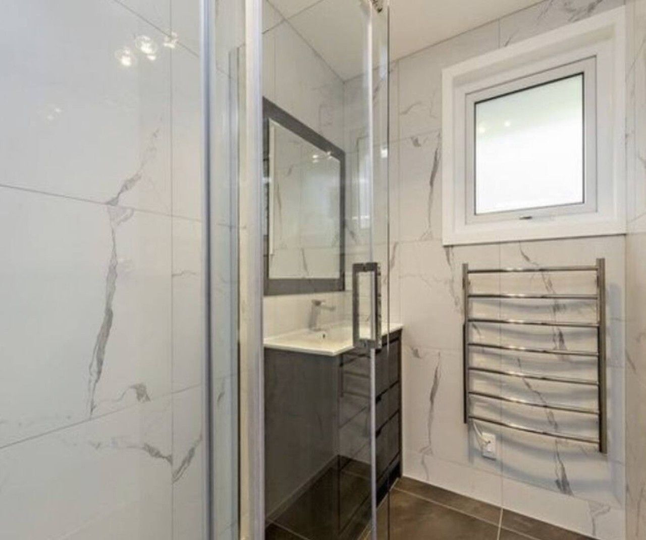 Un baño con cabina de ducha de vidrio, espejo, toallero y ventana.