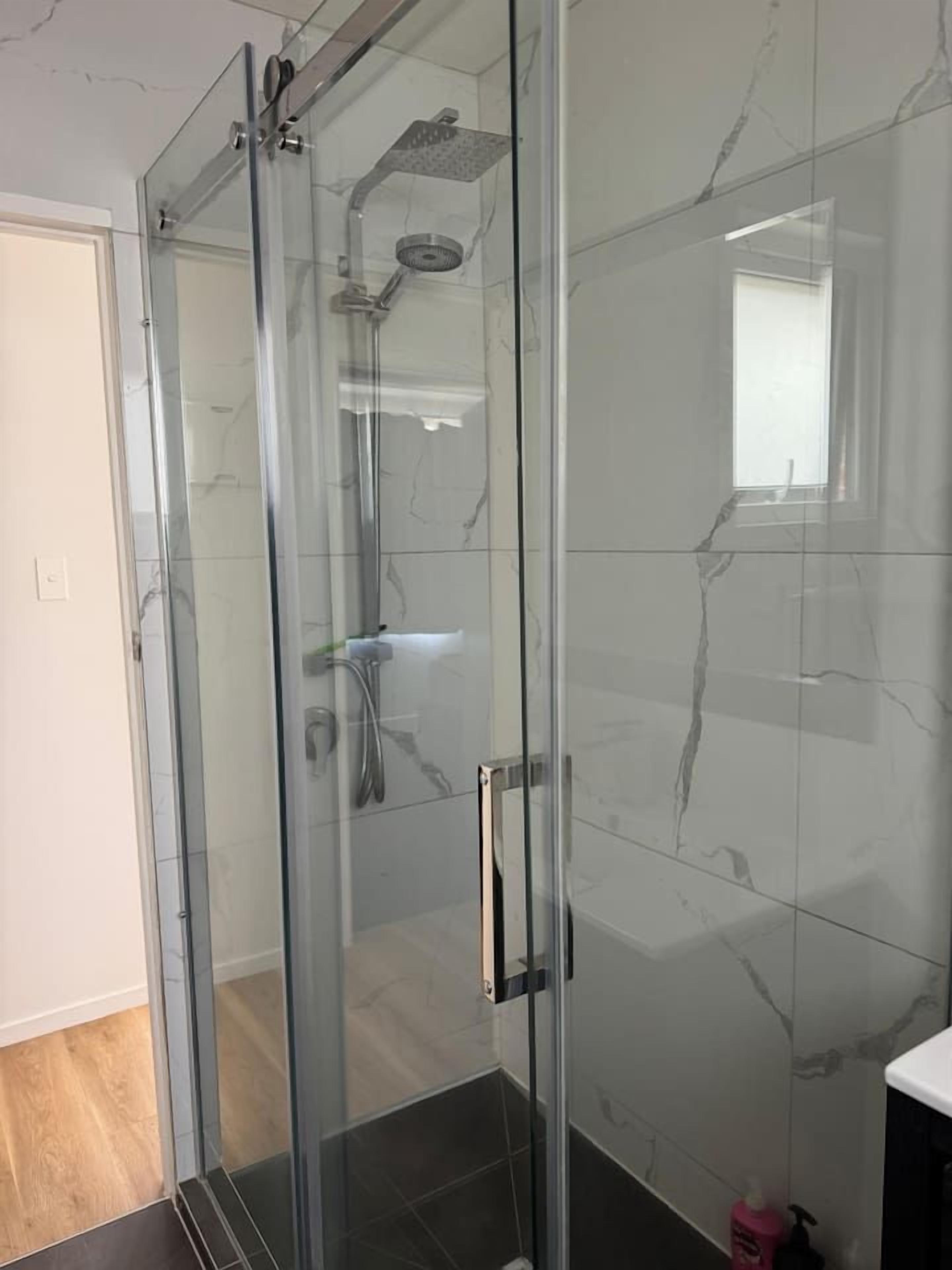 A glass-enclosed shower with a handheld showerhead and a wall-mounted faucet.