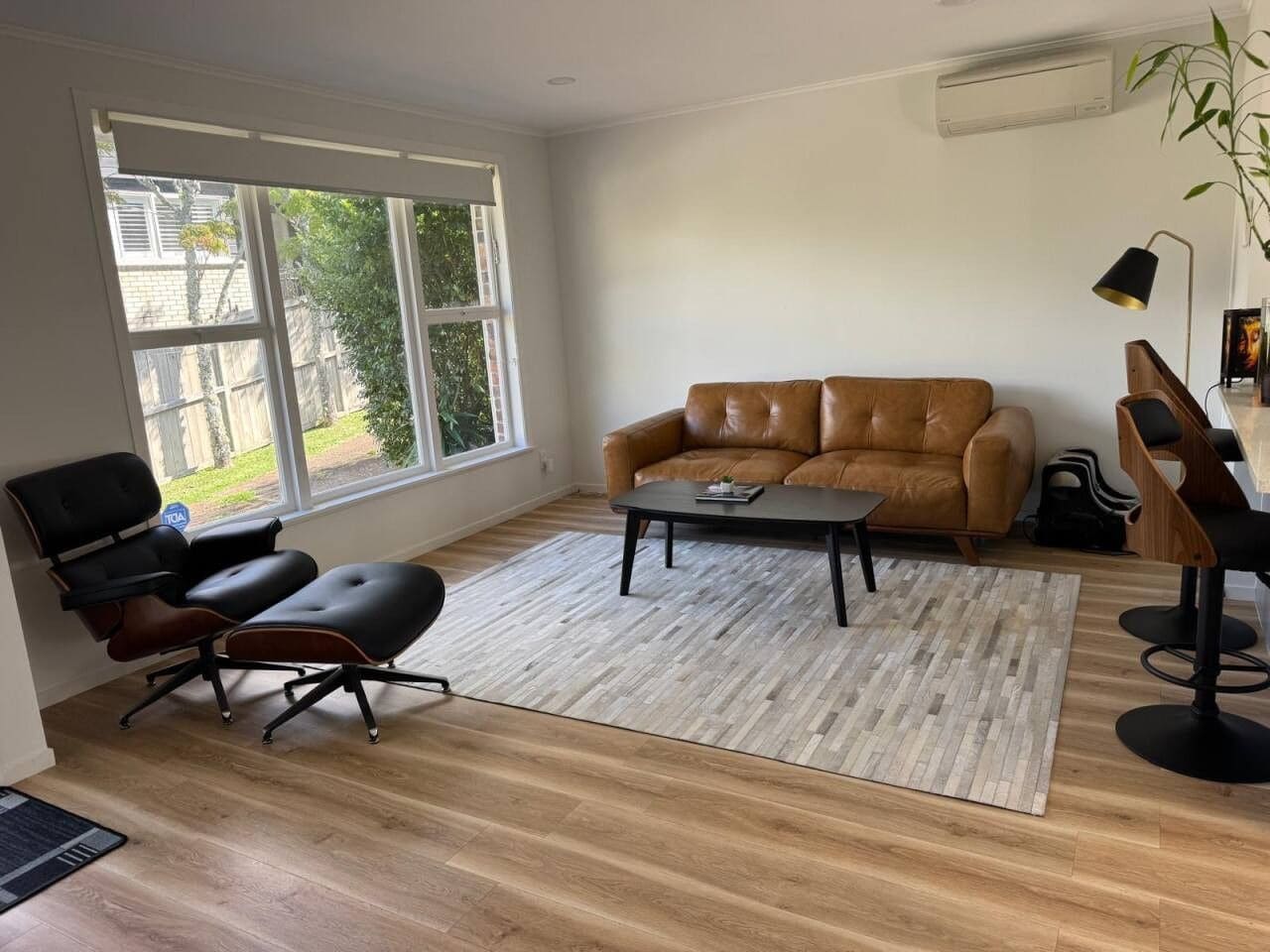A living room with a brown leather sofa, a black office chair, a coffee table, and a wooden floor.