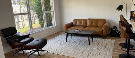 A living room with a brown leather sofa, a black office chair, a coffee table, and a wooden floor.