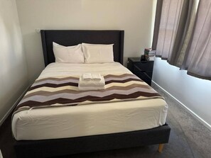 Una cama con cabecera oscura, almohadas blancas y una colcha a rayas.