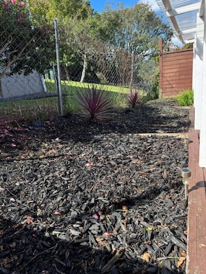 Ein Gartenbereich mit Mulch, einem Holzzaun und Pflanzen.