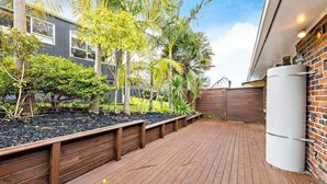 A wooden deck with raised garden beds, a brick wall, and a water tank. - Cosy 2-Bedroom holiday home in Auckland (Saint Heliers)