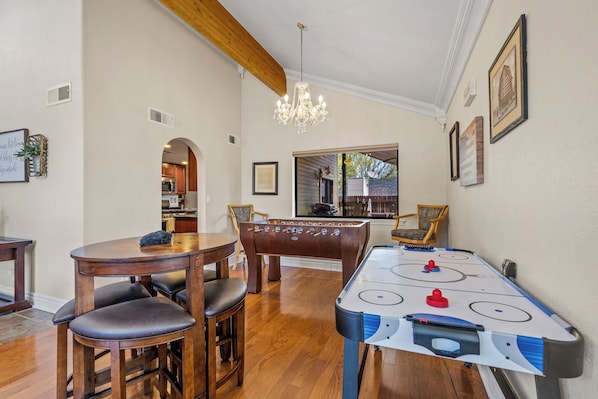 Una habitación con una mesa de madera, sillas, una mesa de futbolín y una mesa de billar.