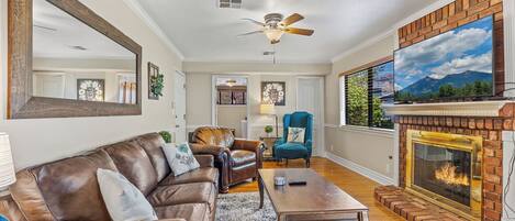 A living room with a fireplace, leather sofa, and a ceiling fan.