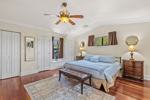 Une chambre à coucher comprenant un lit, un banc, un ventilateur de plafond, une commode et une fenêtre avec des rideaux.
