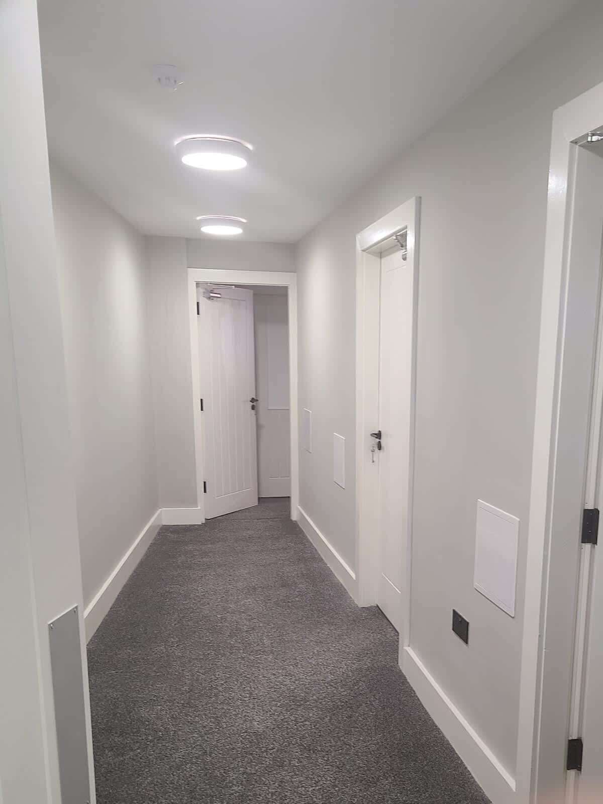 A narrow hallway with white walls, grey carpet, and white doors.