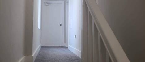 Un couloir étroit, avec un revêtement de sol en moquette, des murs blancs et une porte blanche au fond.