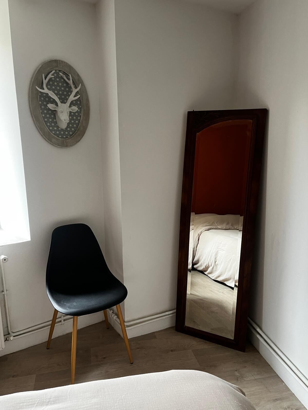 A room with a bed, a chair, a mirror, and a wall-mounted deer head decoration.