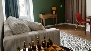 A living room with a sofa, a wooden side table, a red chair, a chessboard, and a patterned rug. - Charming apartment - historic heart of Aubusson (Aubusson)