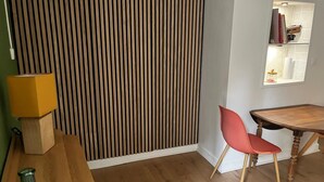 A room with a wooden floor, a wooden table, a red chair, a yellow lamp, and a wooden partition with vertical slats. - Charming apartment - historic heart of Aubusson (Aubusson)