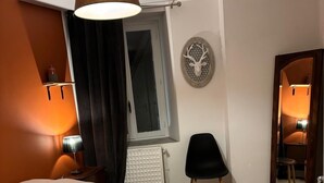 A bedroom with a bed, a chair, a mirror, a wall-mounted lamp, and a radiator. - Charming apartment - historic heart of Aubusson (Aubusson)
