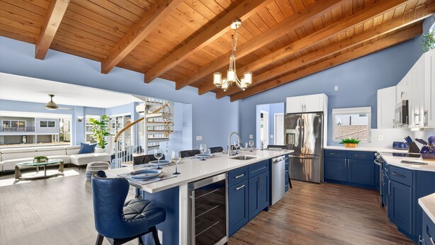 Una cocina moderna con una isla grande, vigas de techo de madera y vistas al área de estar.