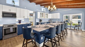 Una cocina moderna con armarios blancos, una isla central con taburetes y un techo de madera.
