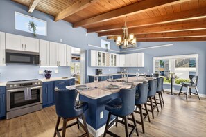 A modern kitchen with white cabinets, a central island with bar stools, and a wooden ceiling. - Blue Bay View - Canal Front- Heated Pool (Fort Myers Beach)
